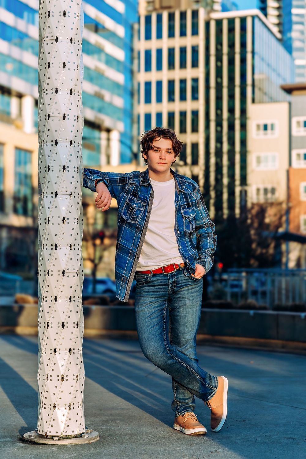 Urban fashion poses with denim outfit against white columns and city buildings.