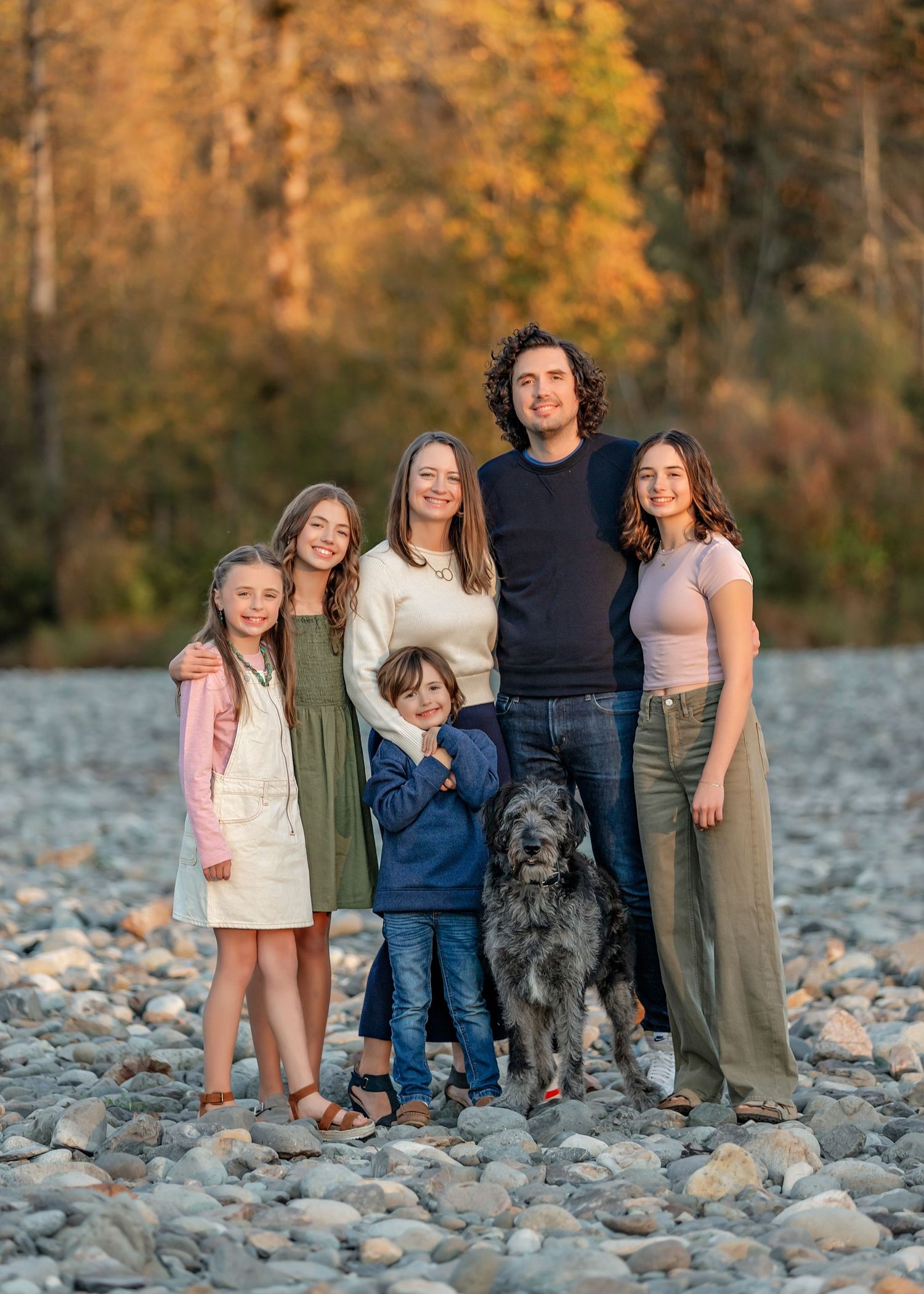 Family with their dog posing together on a rocky riverbank during autumn.