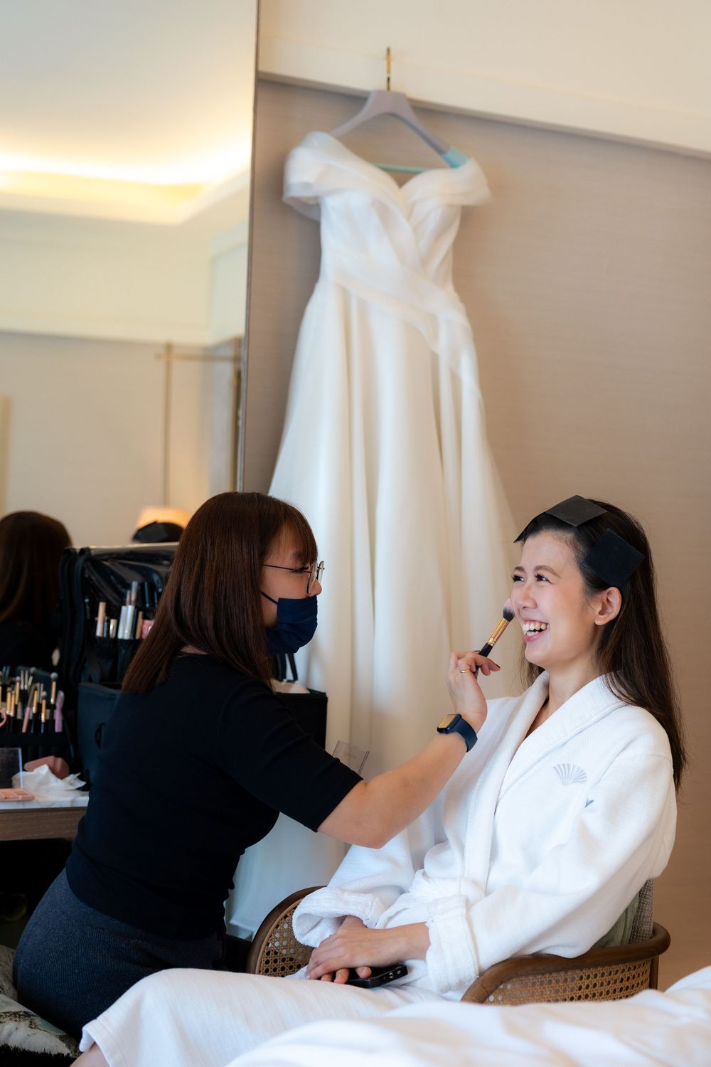 Makeup artist applies cosmetics to someone wearing a white robe during wedding day preparations.