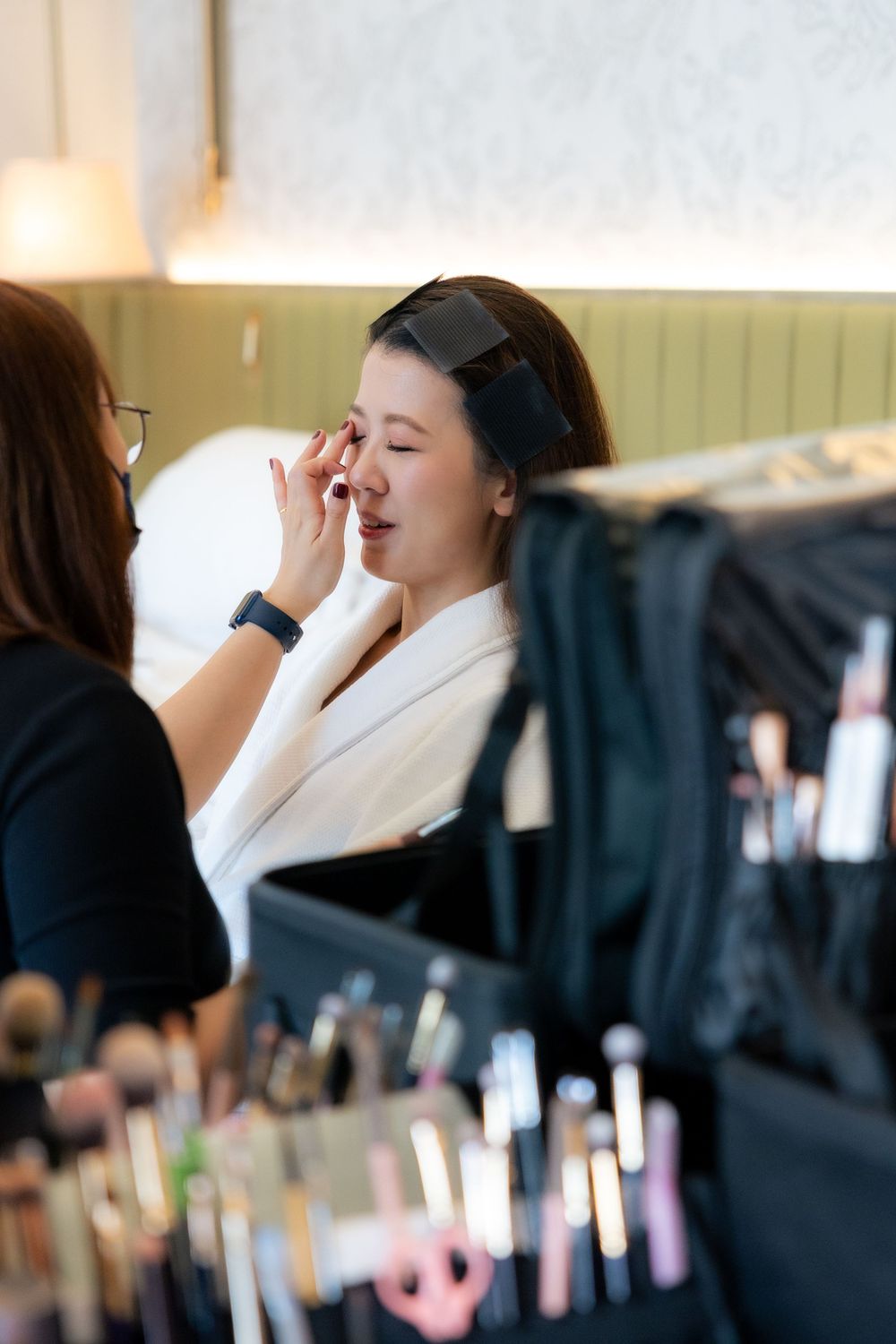 Professional makeup application in progress with artist working on client in white robe.