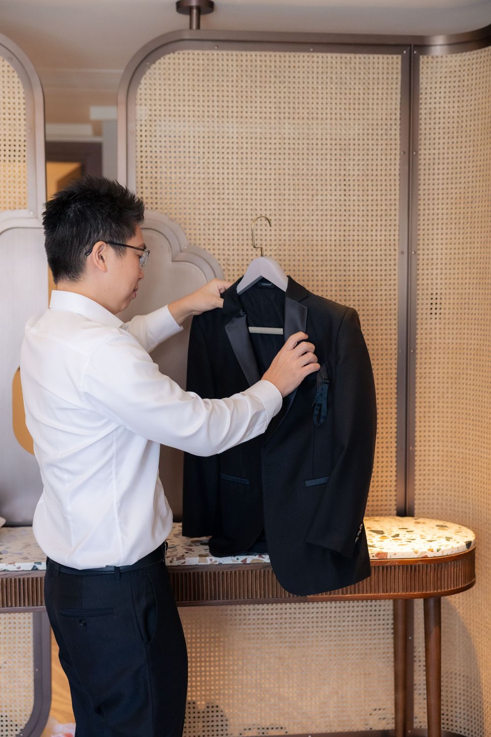 Professional tailor carefully adjusts details on a formal black suit jacket hanging on display.