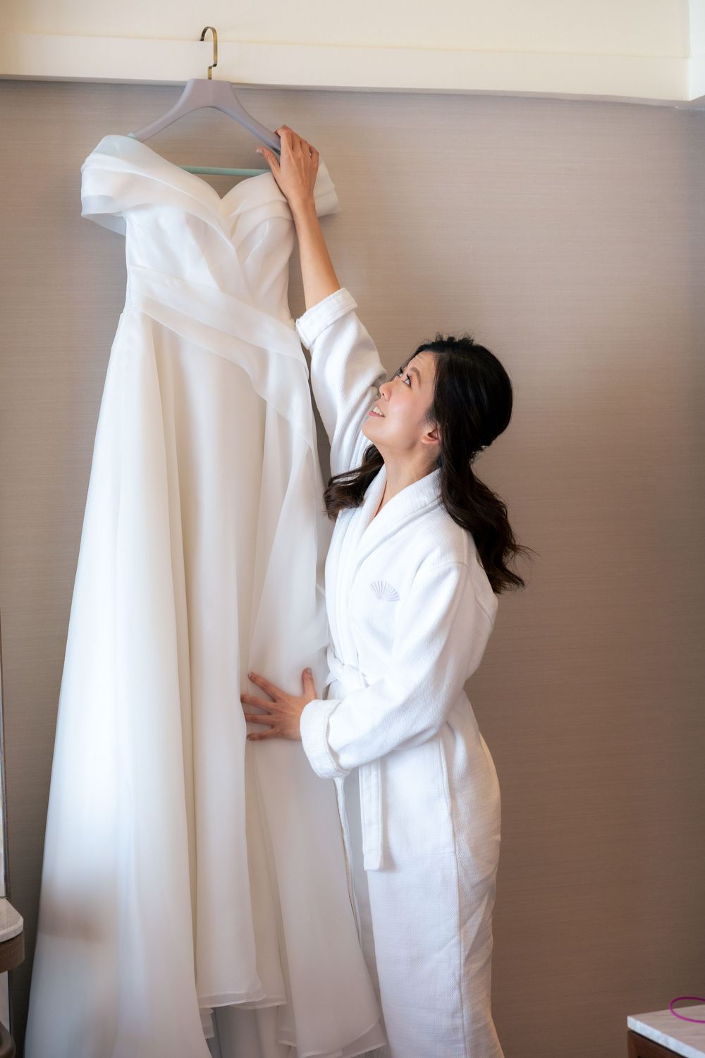 Person in white examining and adjusting a formal white wedding dress on a hanger.