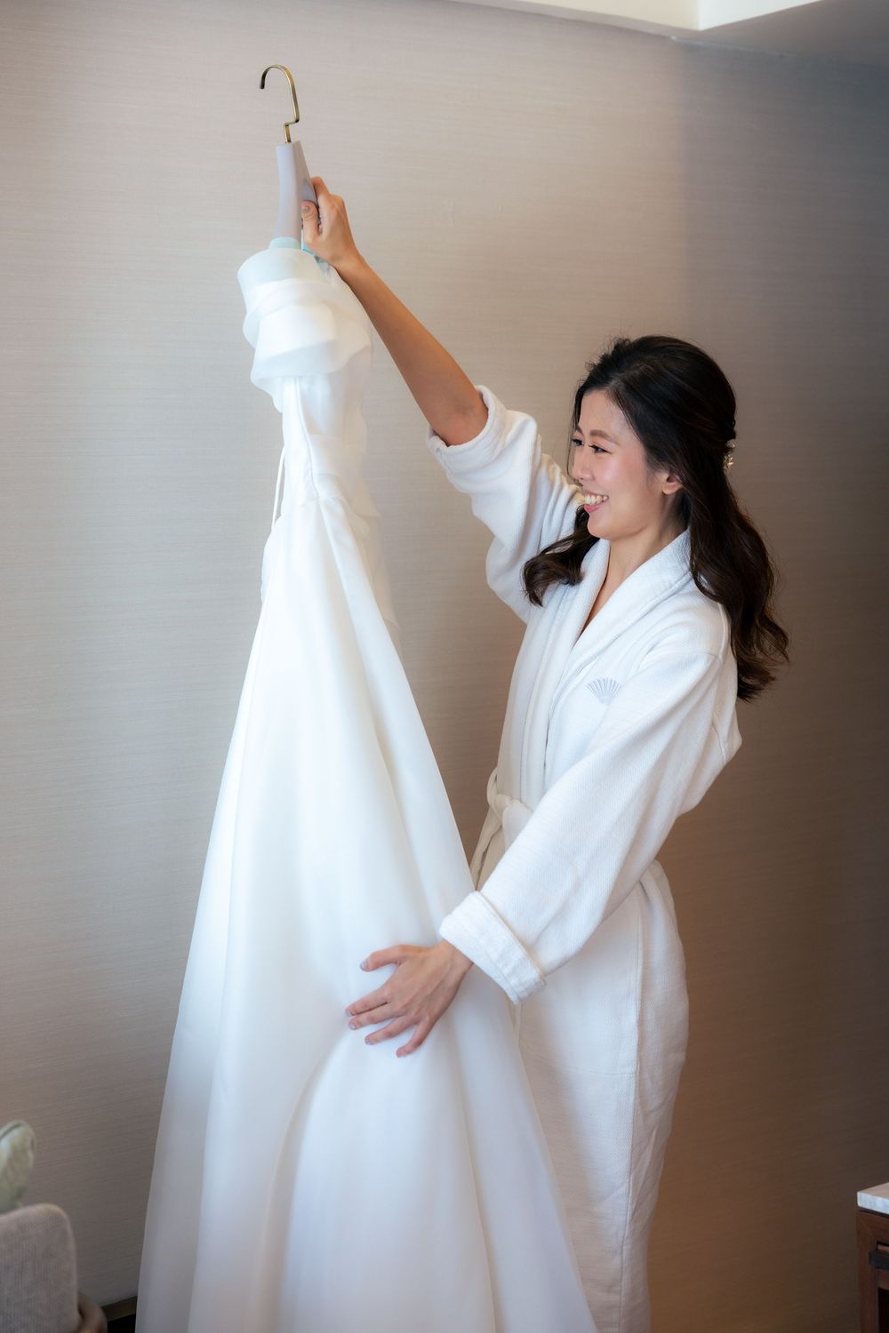 A white wedding dress being held up against natural lighting in a room.