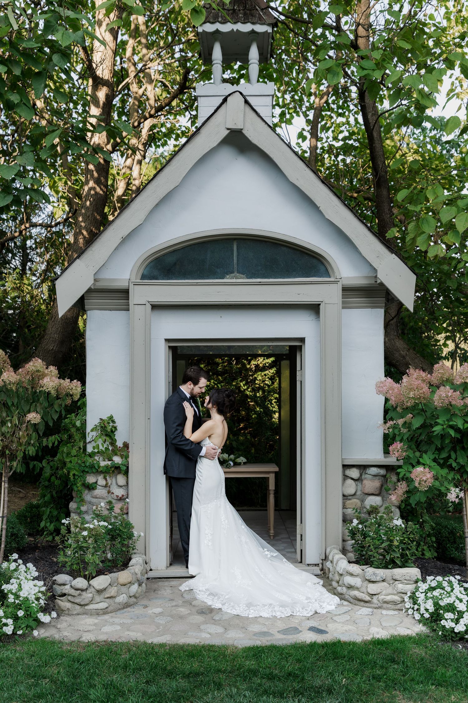 Small chape creates romantic backdrop for wedding couple portraits in garden setting at The Wren House in St. Jacobs, Ontario.