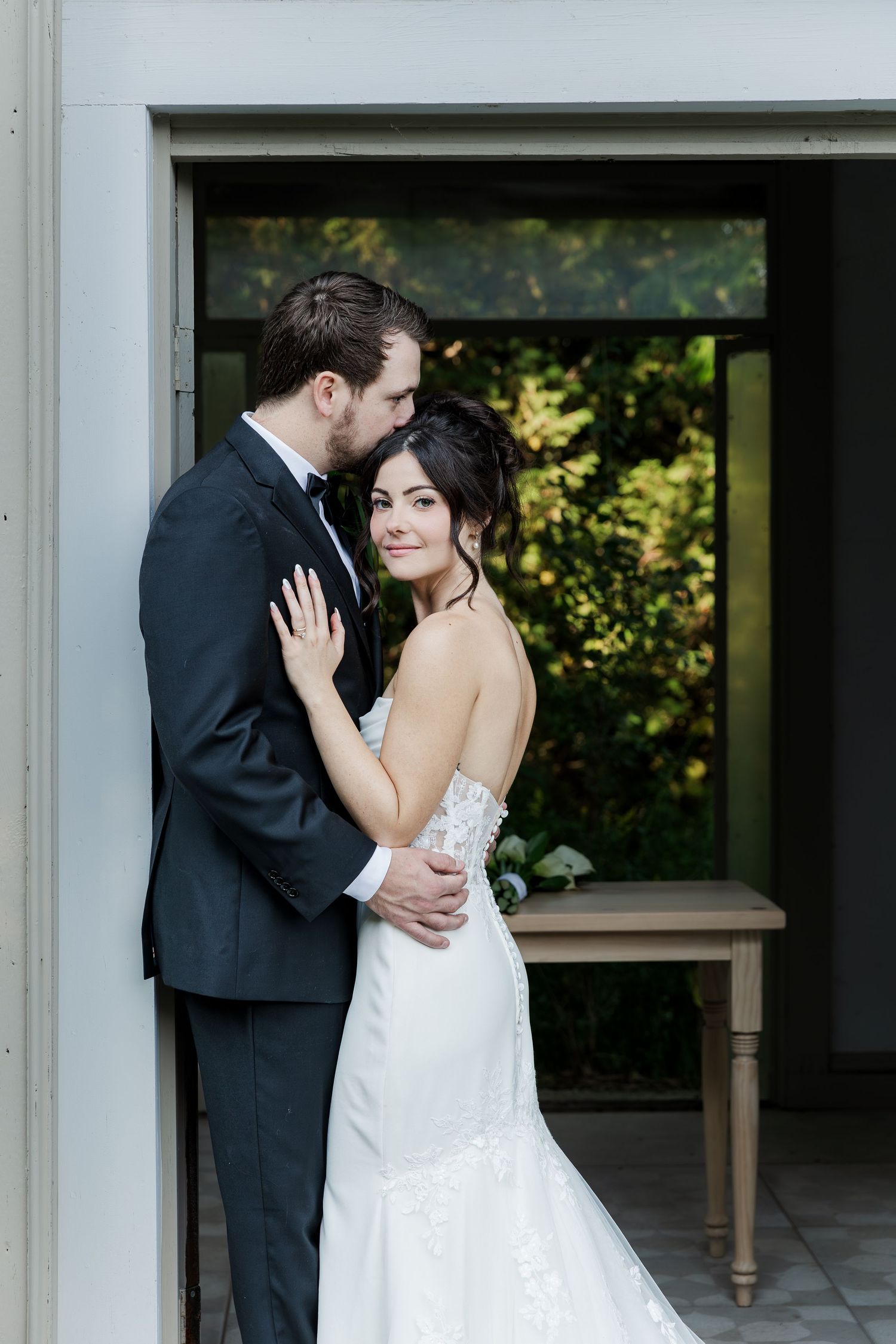 Bride and groom snuggle into each other in the small chapel building surrounded by greenery at The Wren House in St. Jacobs, Ontario.