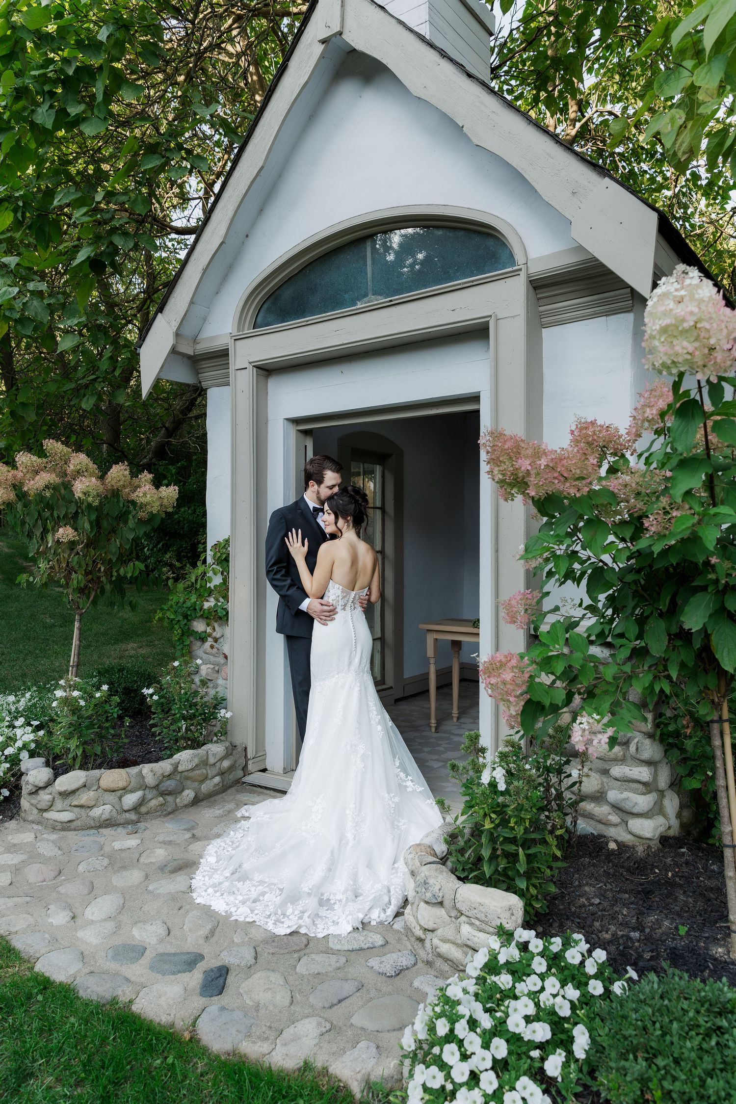 A couple shares a romantic moment in front of a stone church entrance surrounded by lush greenery at The Wren House in St. Jacobs, Ontario.