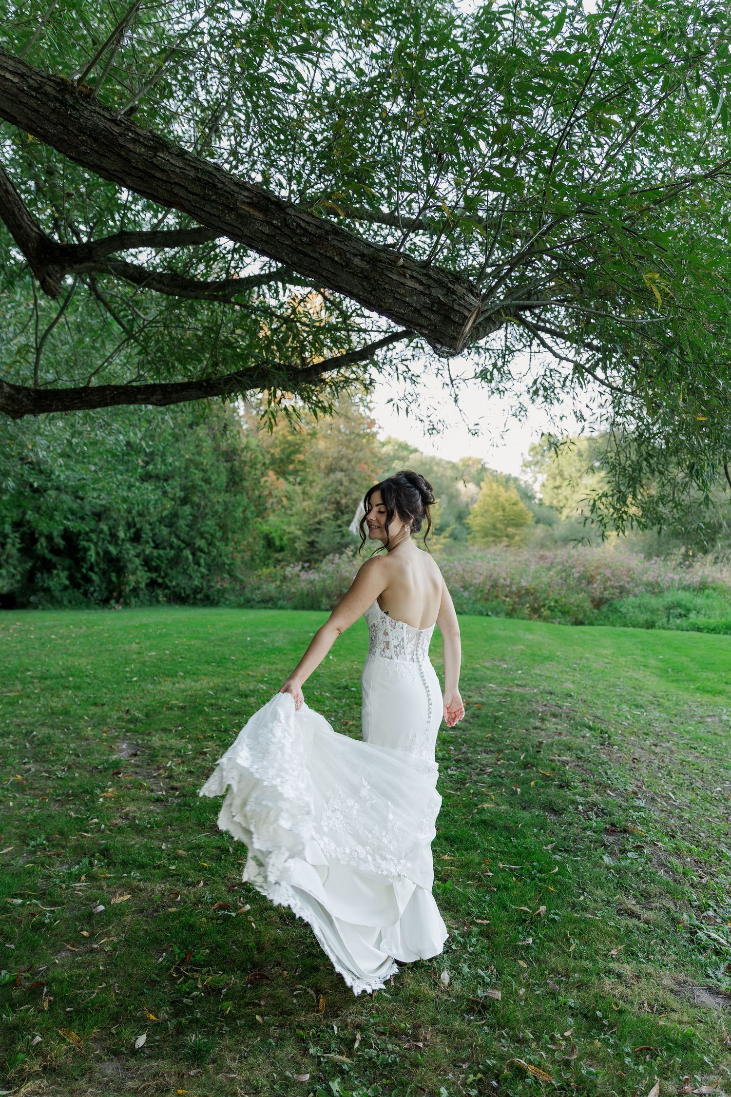 A bride playfully spins in her dress underneath a tree canopy on the riverbank of the grand river at The Wren House in St. Jacobs, Ontario.