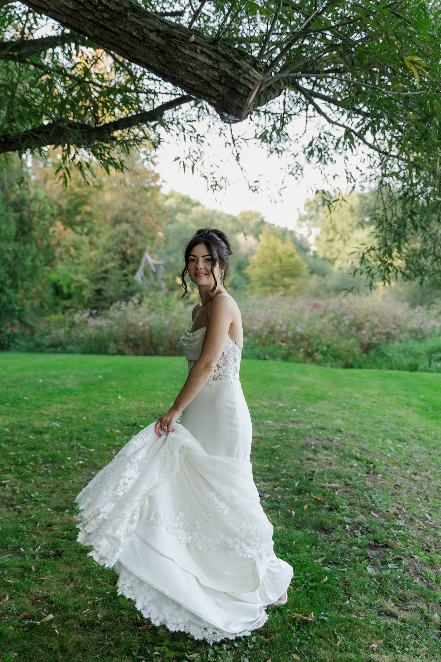 A bride with a flowing white wedding dress twirls under tree branches at The Wren House in St. Jacobs, Ontario.