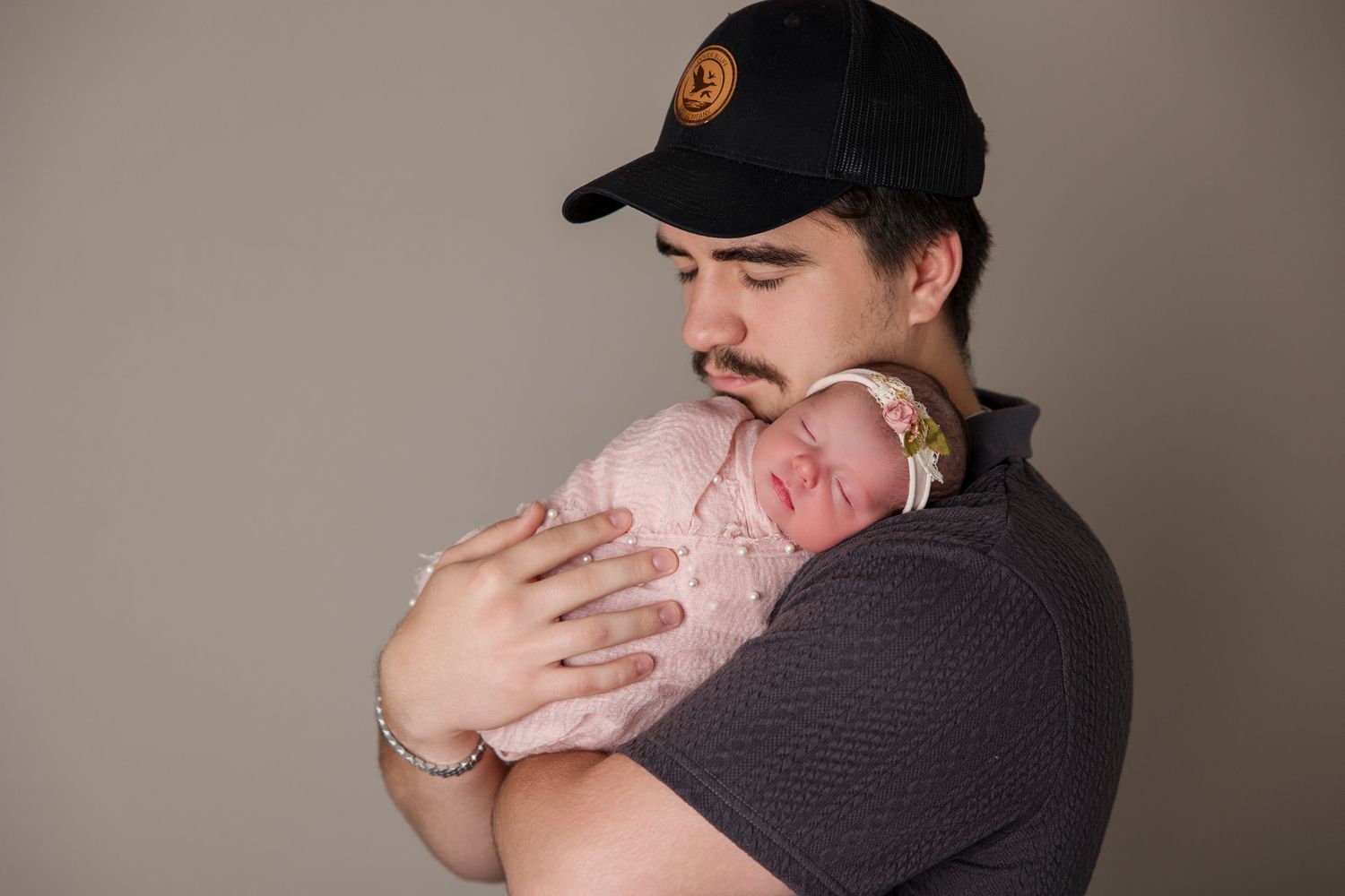 Person in black baseball cap and dark shirt holds and kisses small baby in tender candid photo series.