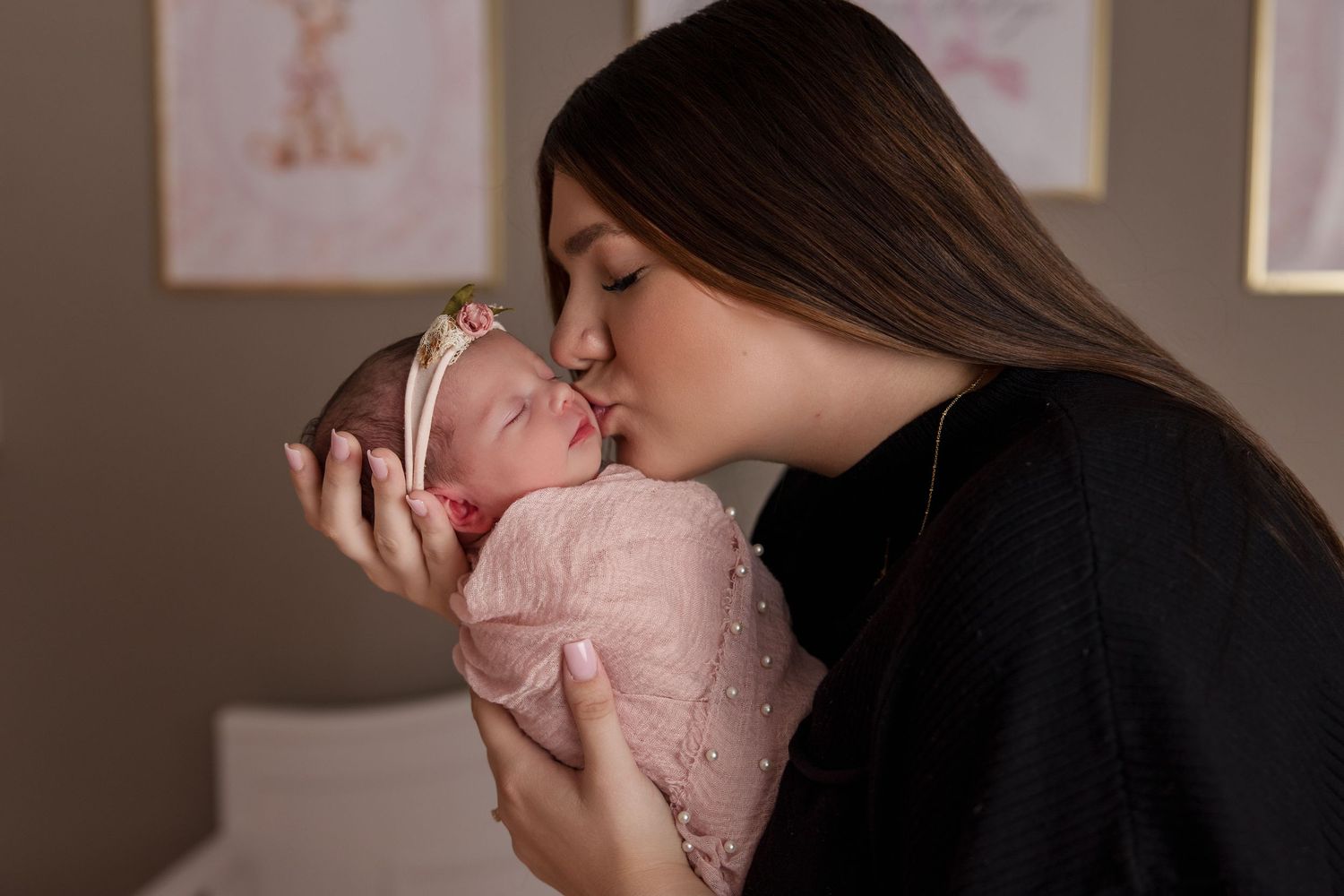 A tender moment between mother and newborn baby in pink clothing during a professional photography session.