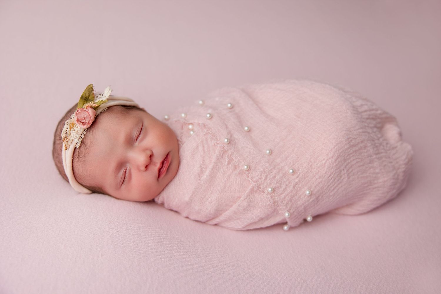 Sleeping newborn wrapped in delicate pink fabric against pink backdrop in professional studio setting.