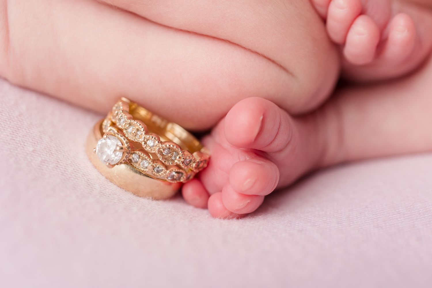 Detail shots of newborn baby's tiny feet and hands with gold ring during professional photo session.