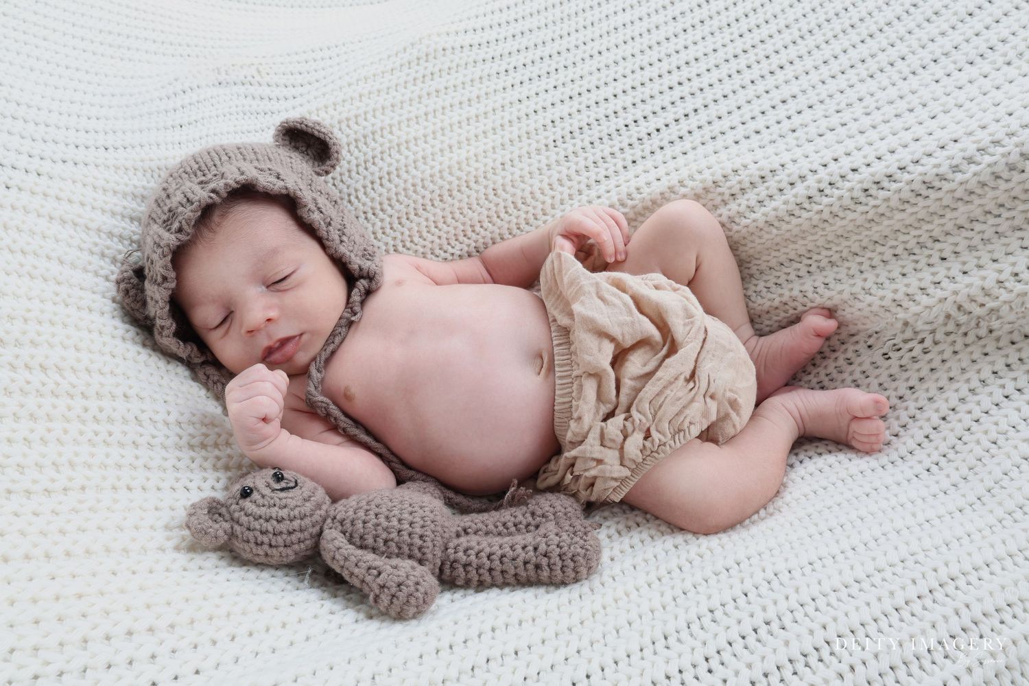 Newborn infant peacefully sleeping on soft white textured blanket wearing cozy knit bonnet.
