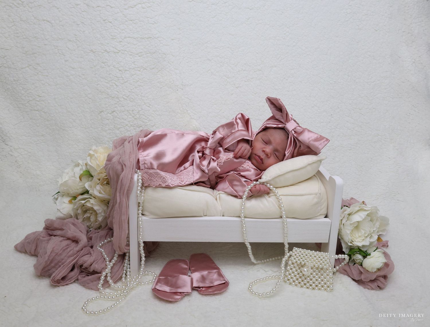 Vintage baby shoes and clothing accessories in soft pink and white tones arranged on white fabric.