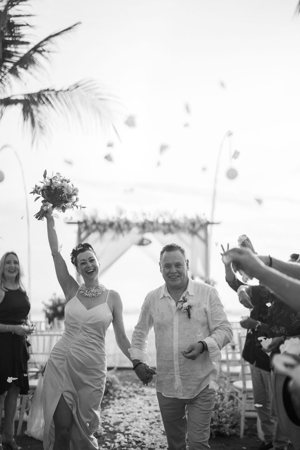 Wedding guests celebrate with joyful dancing and movement on a beach under palm trees.
