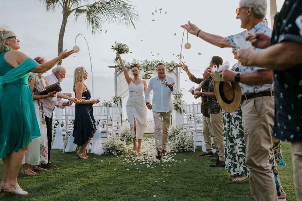Guests enjoying a festive celebration outdoors with raised hands and palm trees in the background.