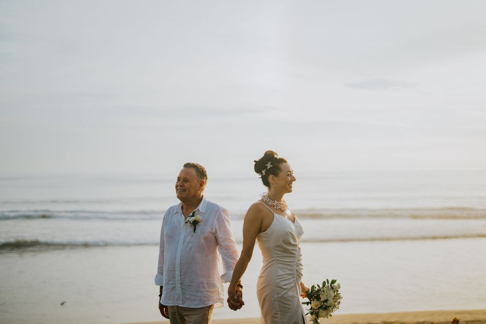 Couple walking along a serene beach at sunset with waves crashing in the background.