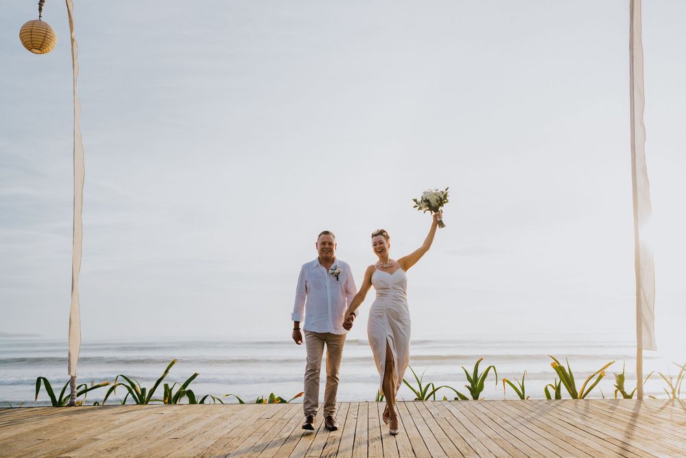 Wedding couple walking on a beach boardwalk surrounded by tropical landscaping.