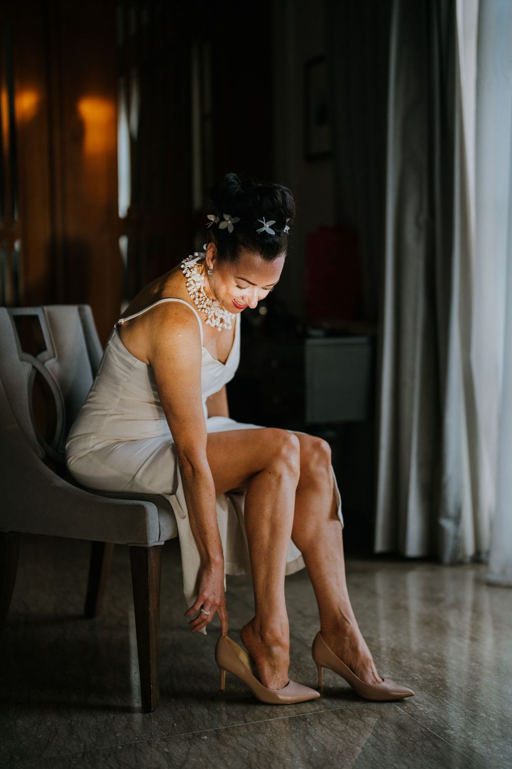 Getting ready scene showing bride putting on wedding shoes in elegant indoor setting.