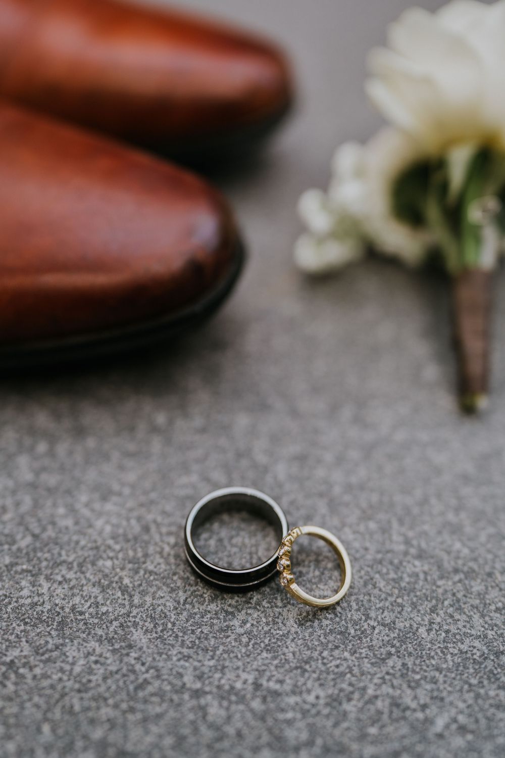 Wedding rings and jewelry arranged on textured gray surface with floral accents.