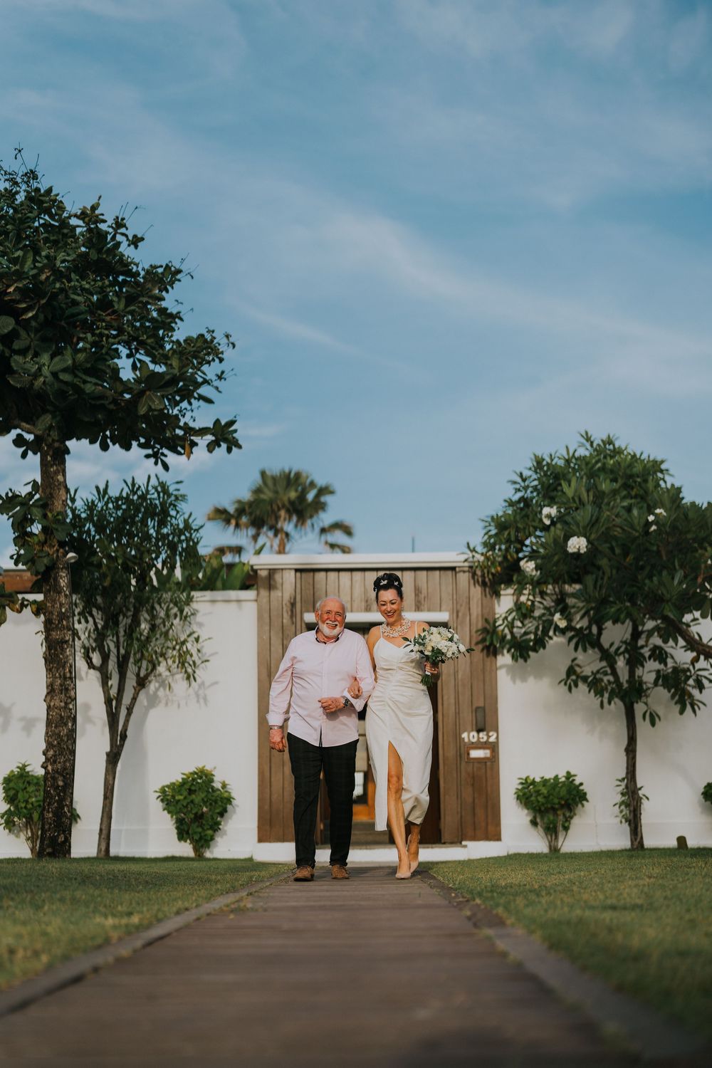 Couple walking together on outdoor path surrounded by trees and blue sky.