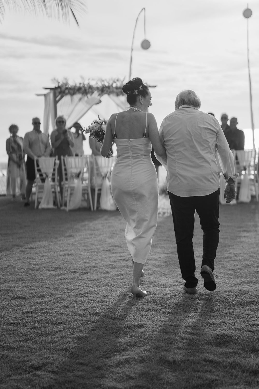 Black and white photo of wedding guests walking across grass during outdoor reception.