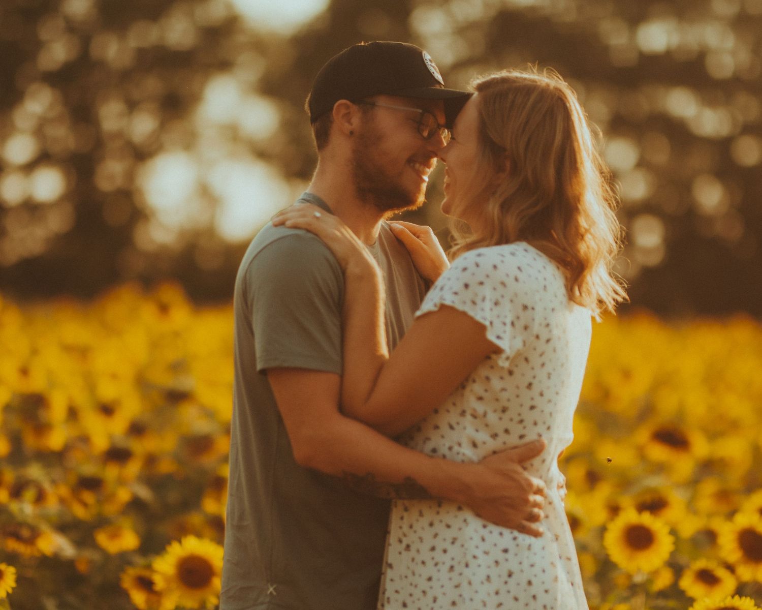Romantic couple embraces in a golden sunflower field at sunset creating a dreamy summer scene.