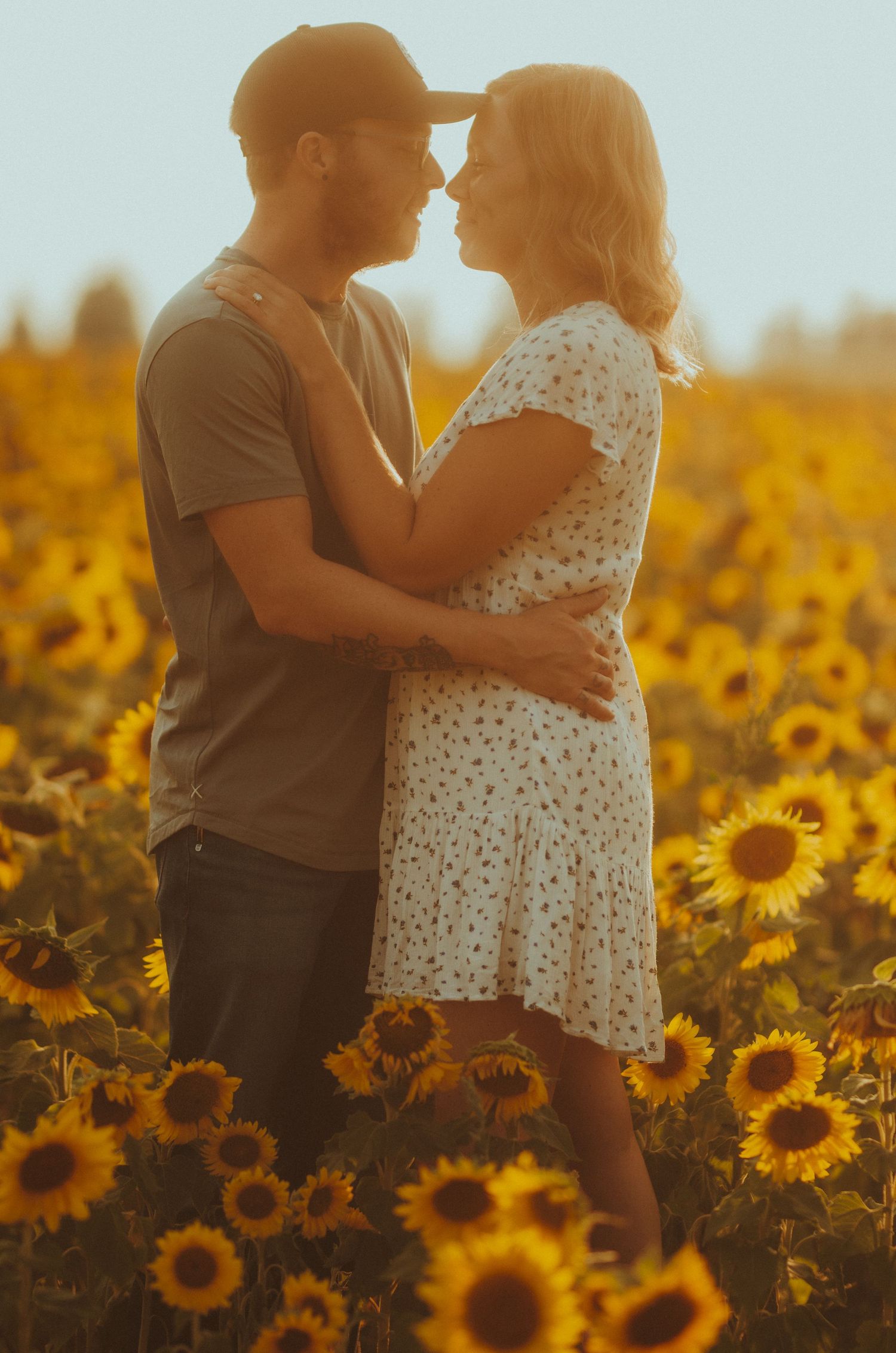 A couple shares a tender moment among vibrant blooming sunflowers at sunset.