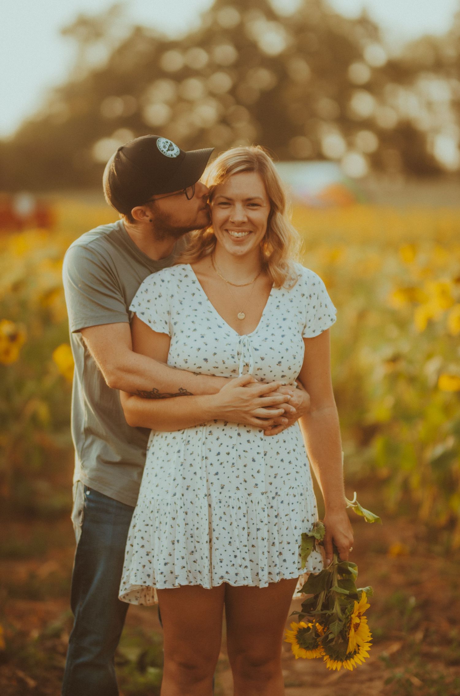 Couple embraces lovingly in golden sunflower field at sunset creating romantic summer portraits.