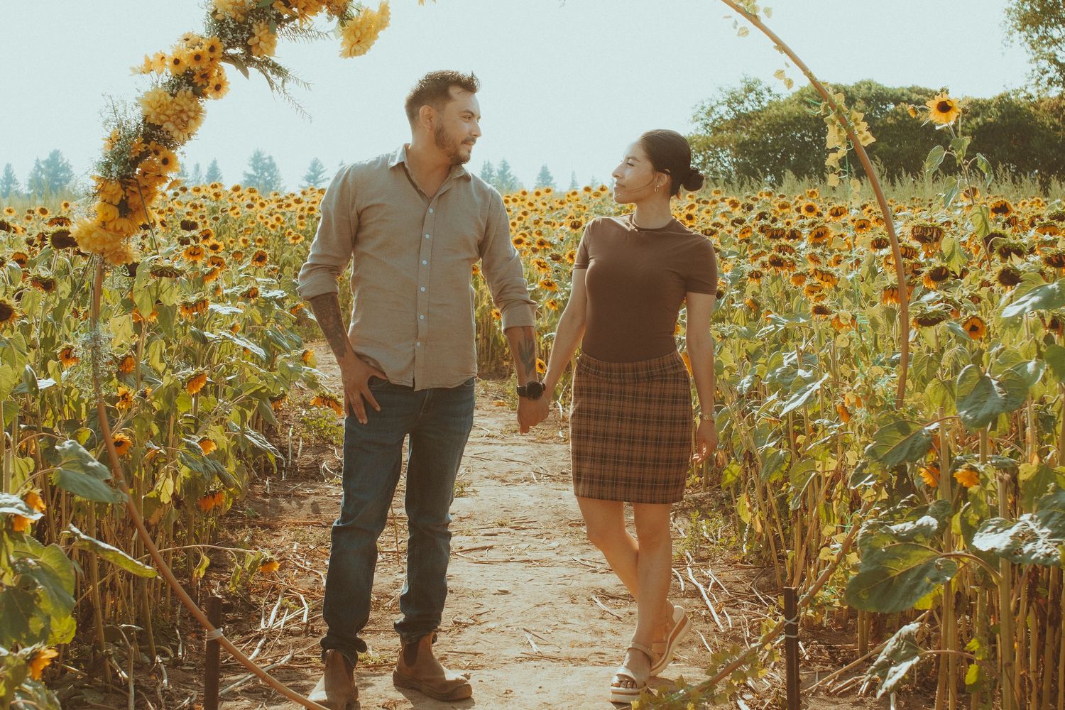 A couple walks through a sun-drenched sunflower field during golden hour on a romantic autumn afternoon.