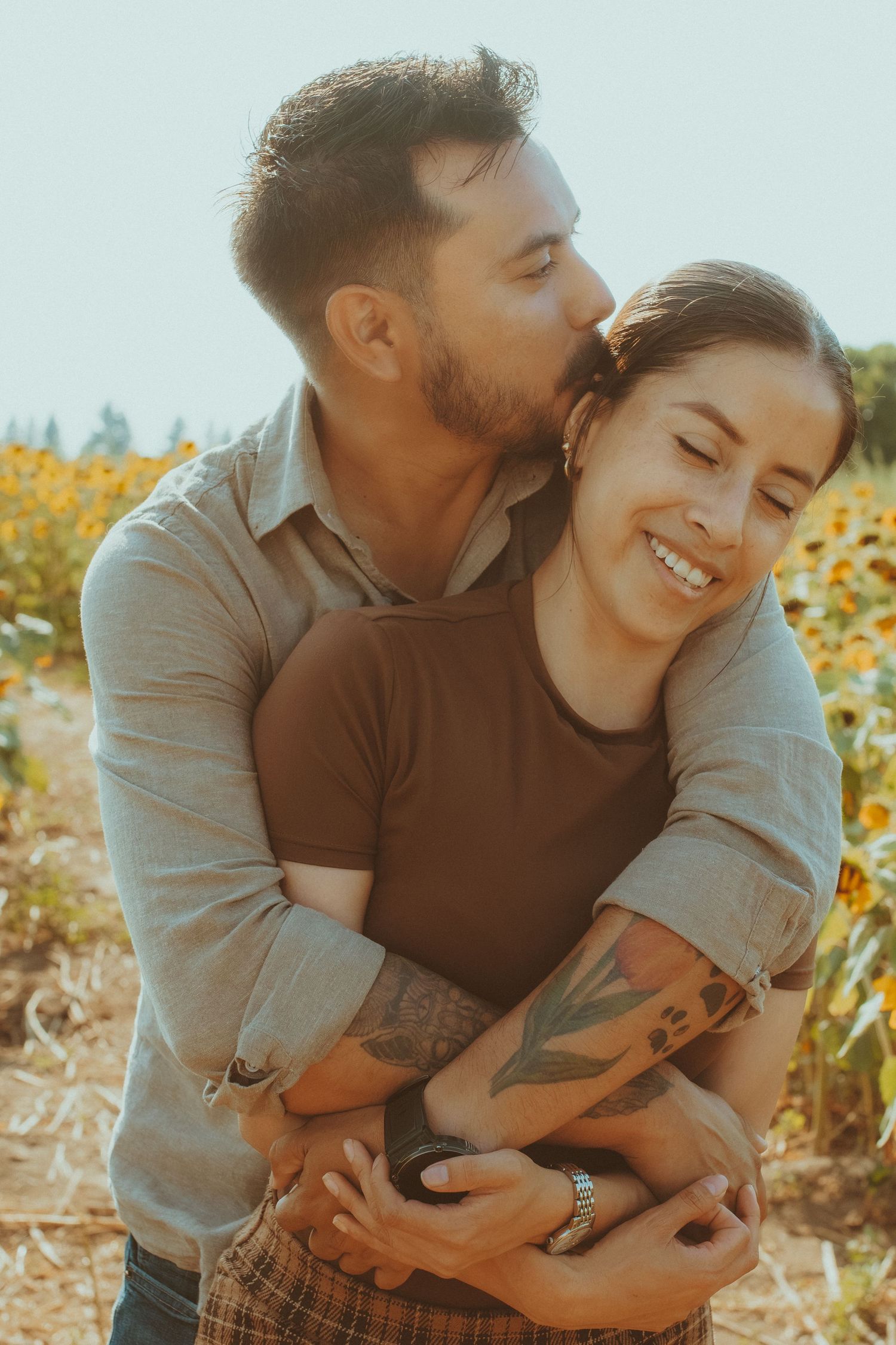 A couple shares tender moments together in a sunny sunflower field on a warm summer day.