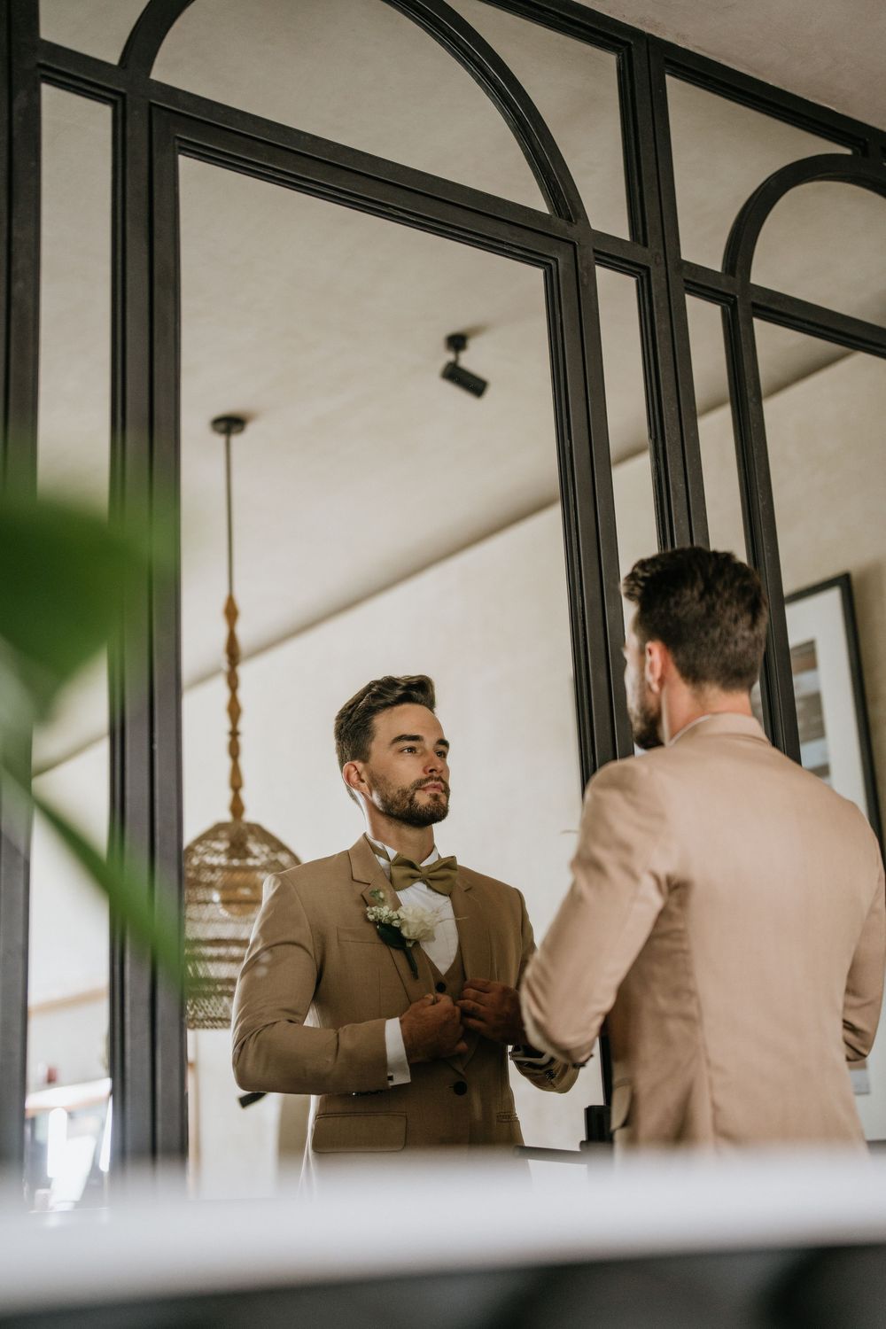 Getting ready scene with formal attire adjustments reflected in arched mirrors.