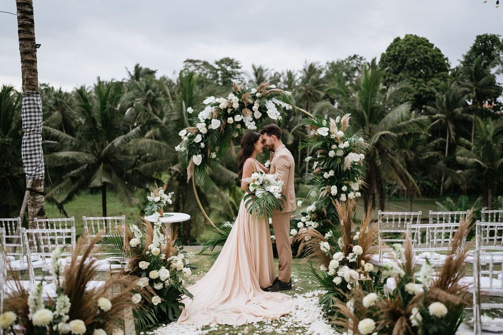 Wedding ceremony space decorated with white flowers and tropical palm trees under cloudy skies.