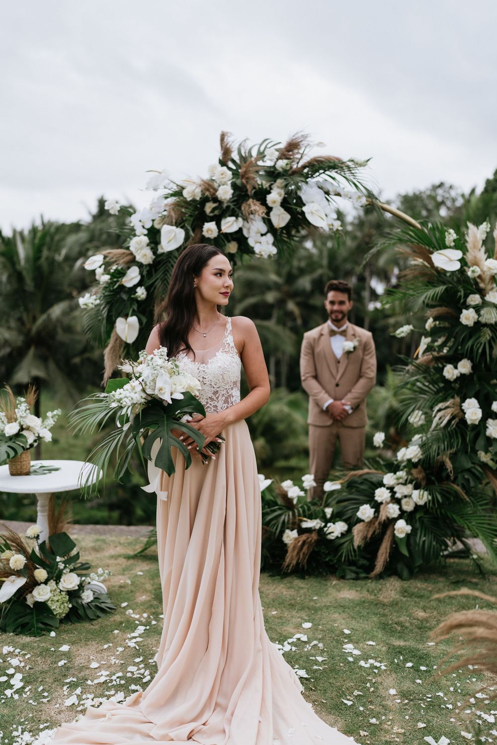 Wedding party in blush and tan attire posing in a lush tropical garden setting.