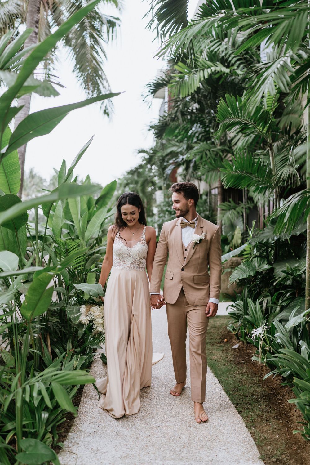 Wedding party walking along a white stone path surrounded by tropical greenery.