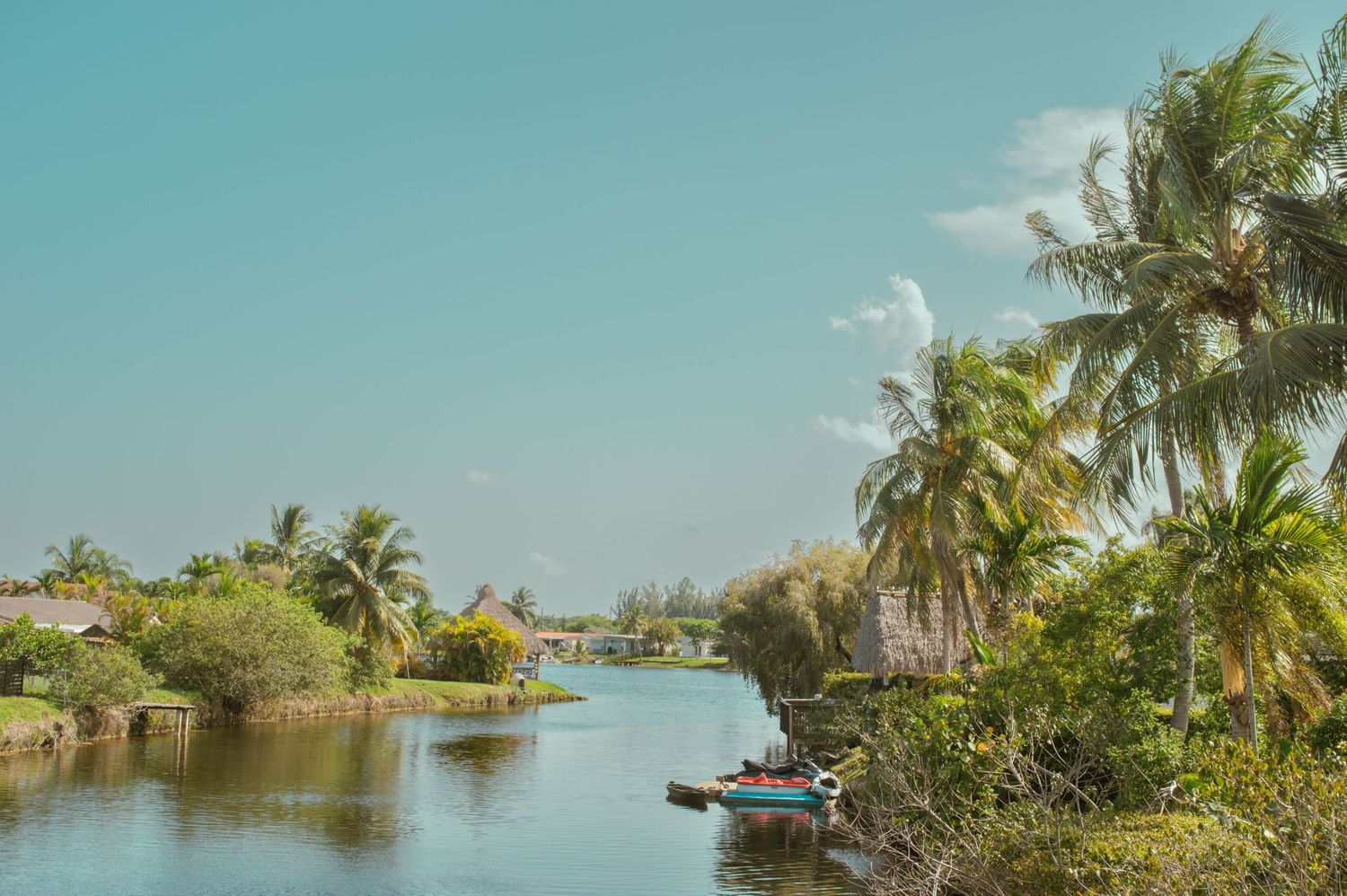 Panoramic view of a tropical waterway with palm trees and boats along a residential waterfront under sunny blue skies.
