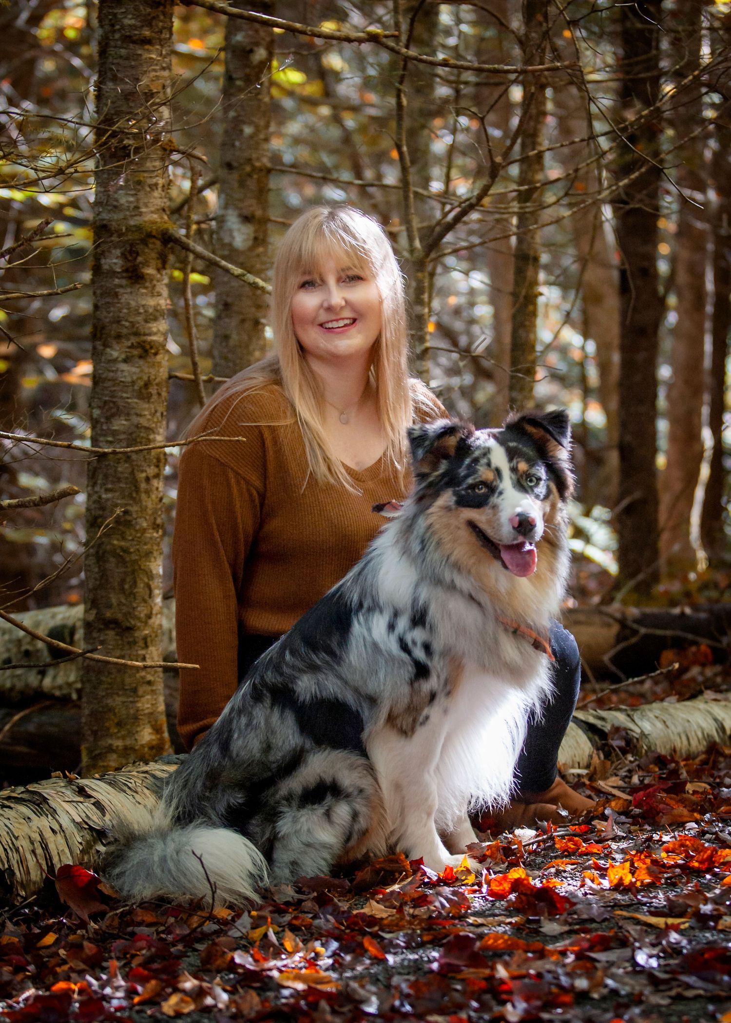 A person sits in autumn forest leaves with their Australian Shepherd dog during a fall photography session.