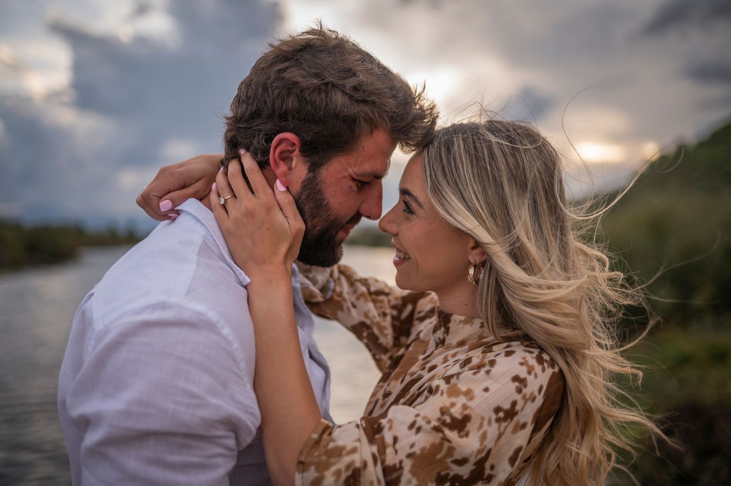 A couple shares a tender moment in a dramatic outdoor setting at sunset with mountains in the background.