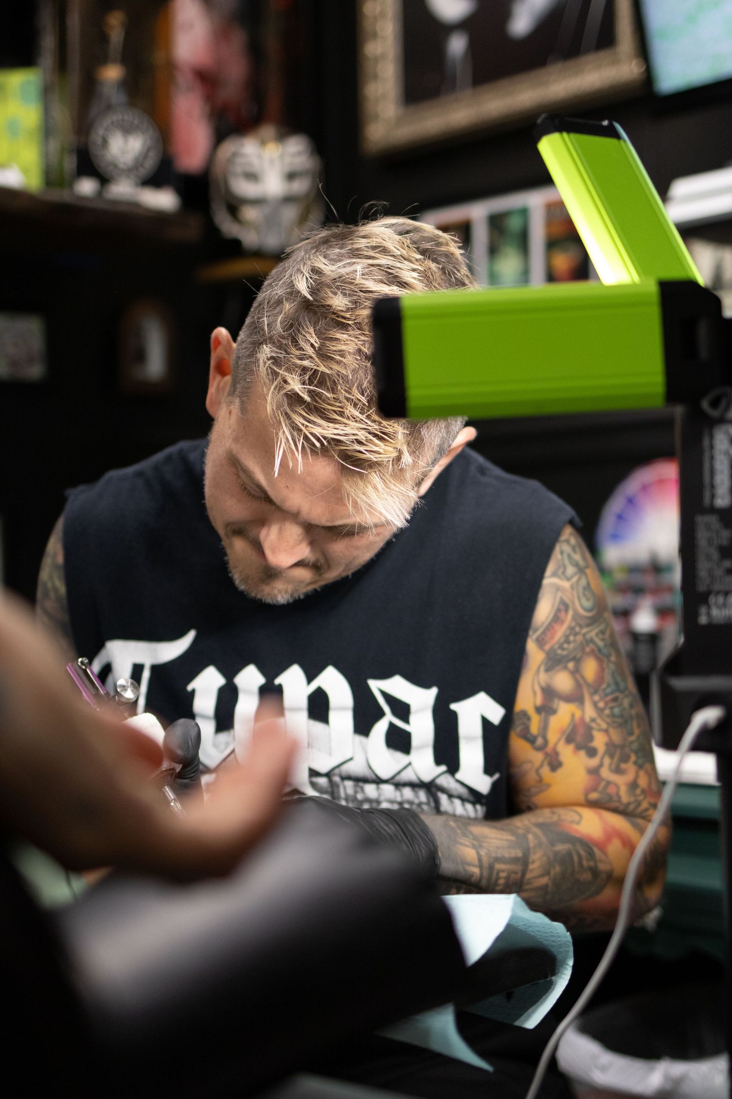 Tattooed person in dark shirt working at desk with focused expression.