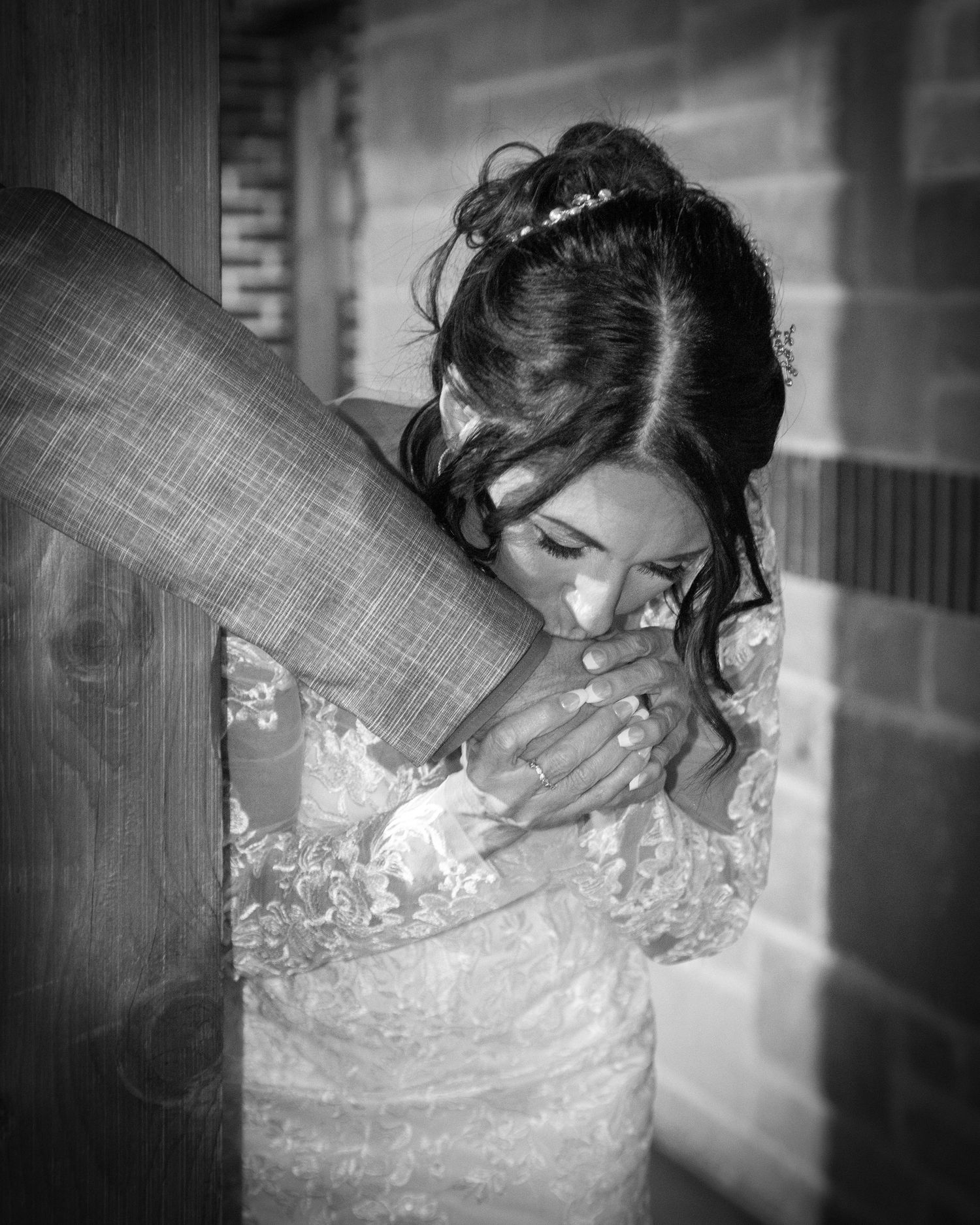 A tender black and white wedding portrait showing an emotional embrace in an intimate brick-walled setting.