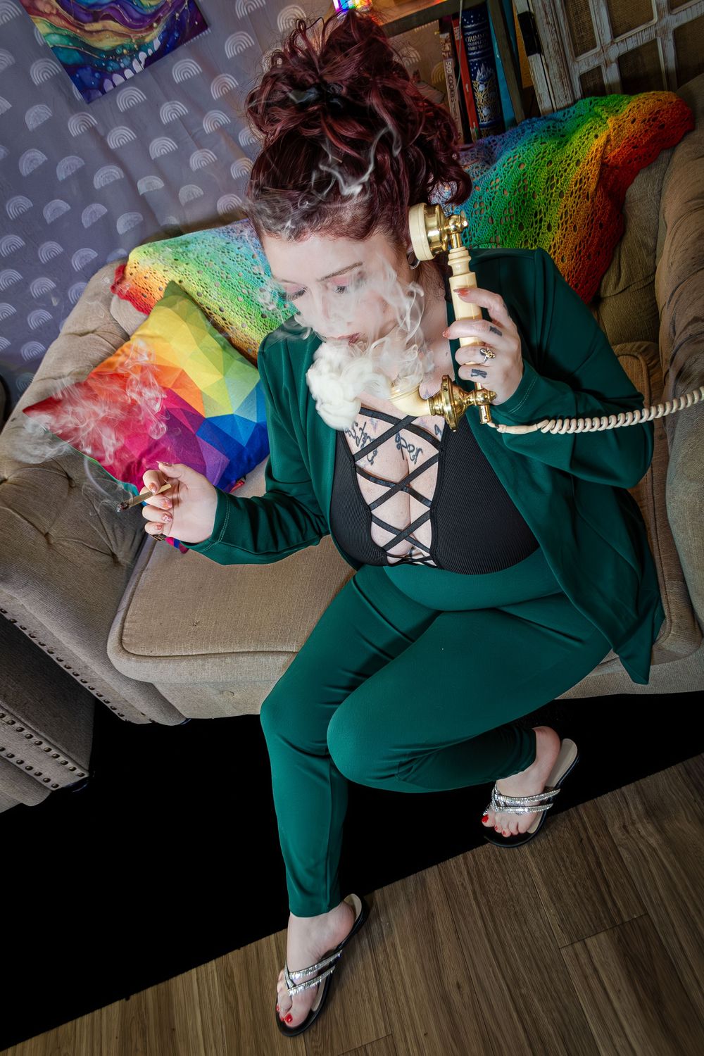 A person in a forest green outfit reclines on furniture with rainbow accent pillows and decorative elements.