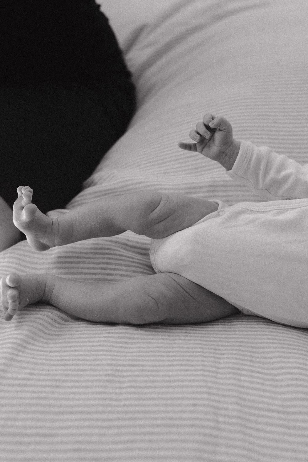 Close-up black and white photo of tiny baby feet and hands on striped bedding.