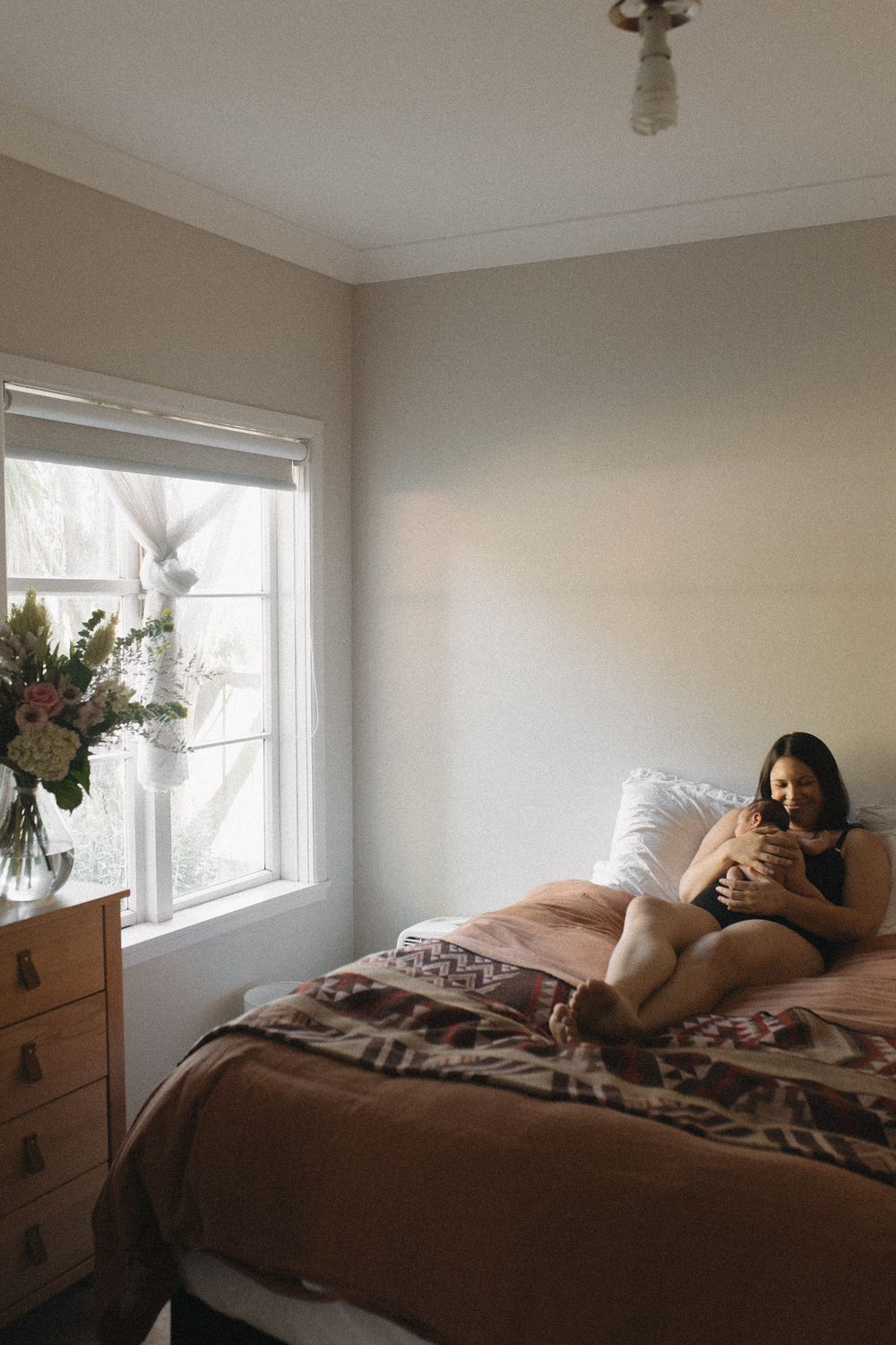 Cozy bedroom scene with natural light streaming through window and floral arrangement on dresser.
