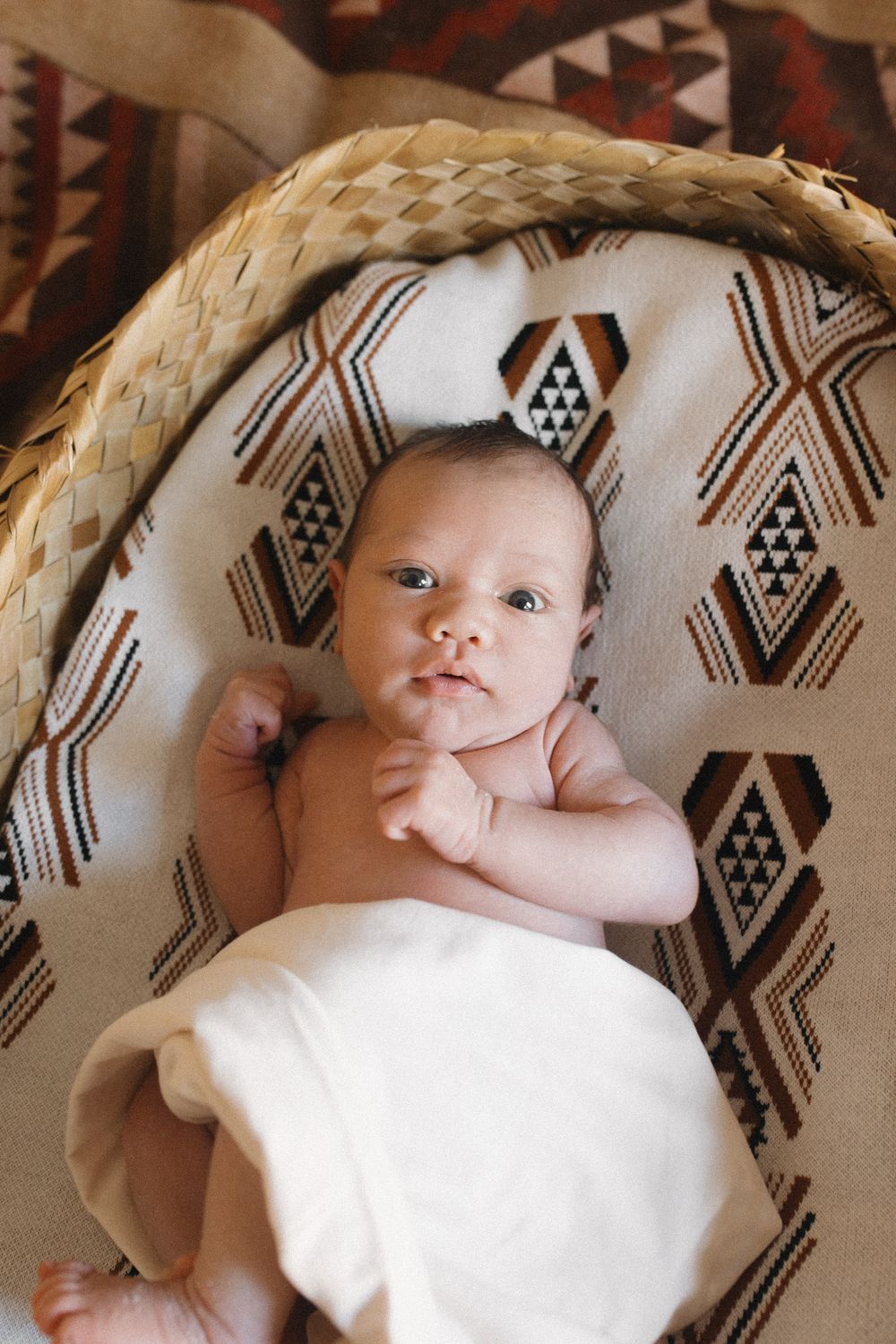 Baby laying on a patterned blanket with geometric tribal designs in earth tones.