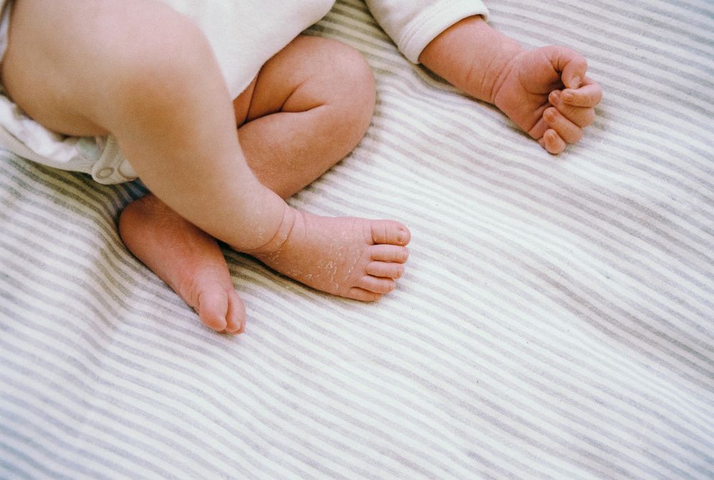 Close up view of tiny baby feet against white striped bedding linens.