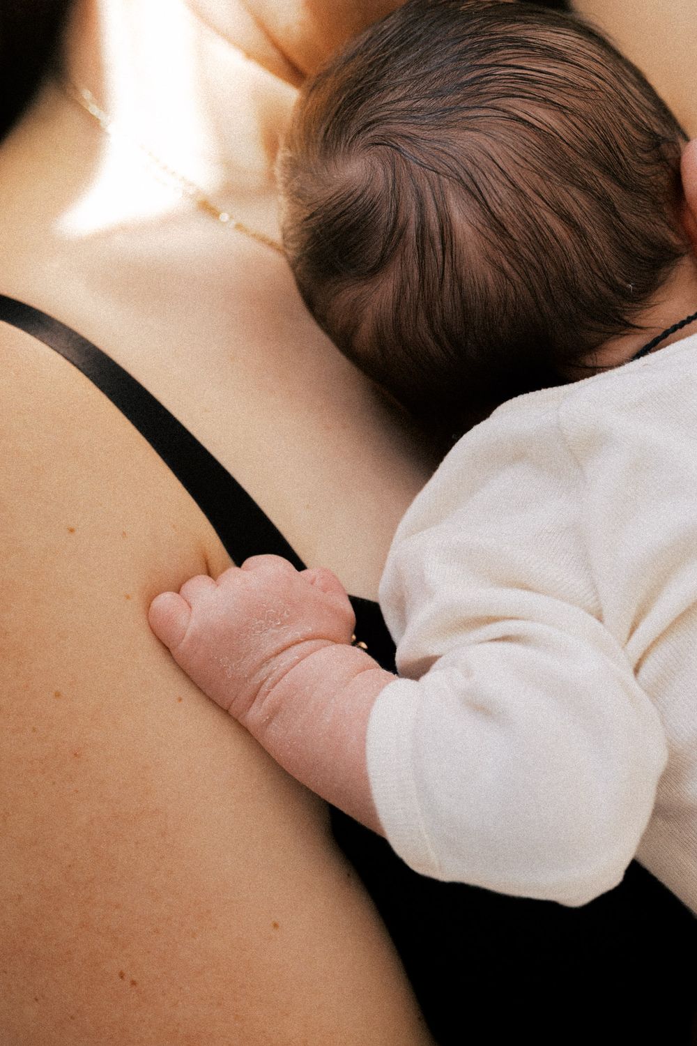 Intimate series of a newborn breastfeeding in natural lighting against soft white fabric.