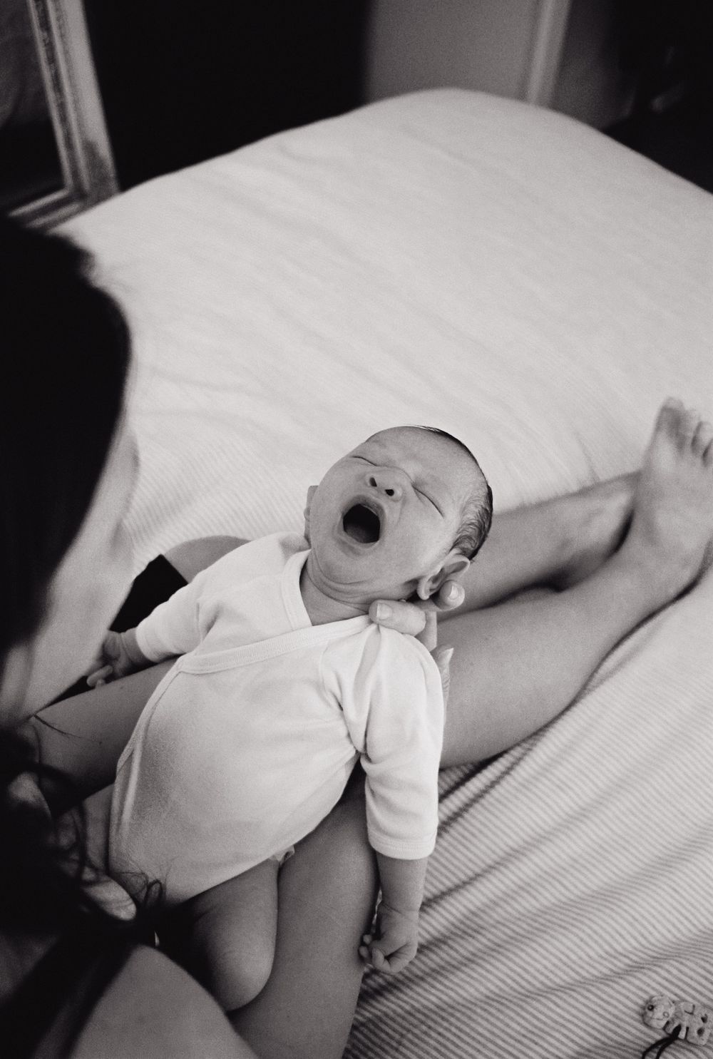Black and white image of a sleeping infant wearing white clothes on white bedding.