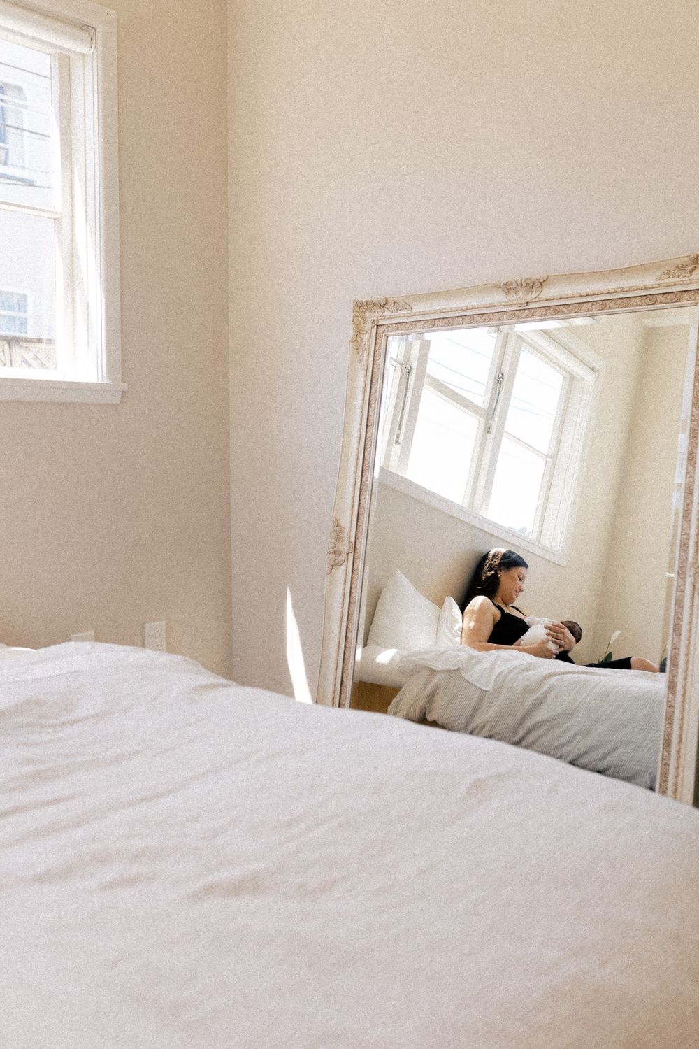 Person sleeping peacefully in light-filled white bedroom with soft bedding and multiple windows.