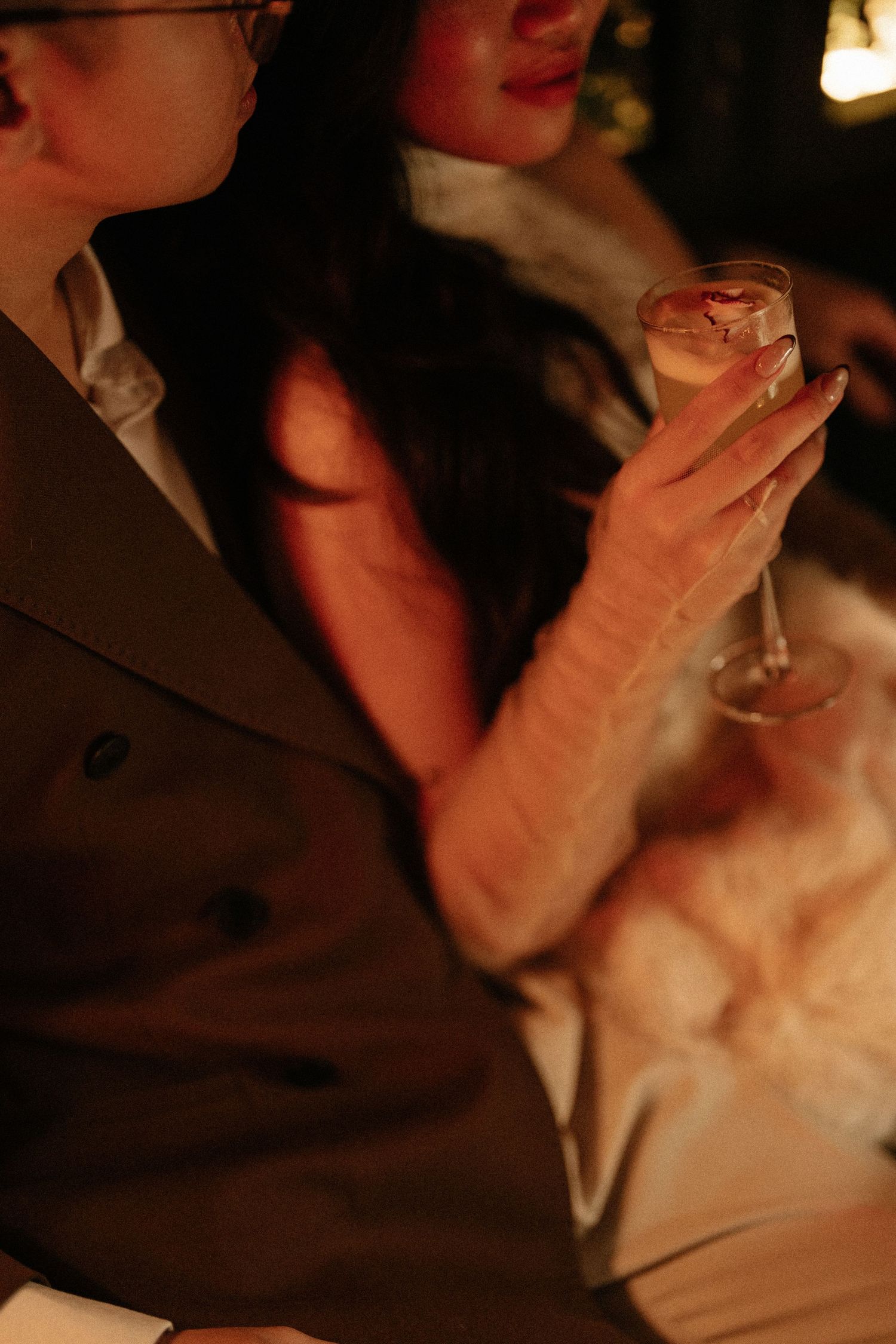 Close-up of a couple in warm candlelight, woman holding a champagne glass in elegant attire.
