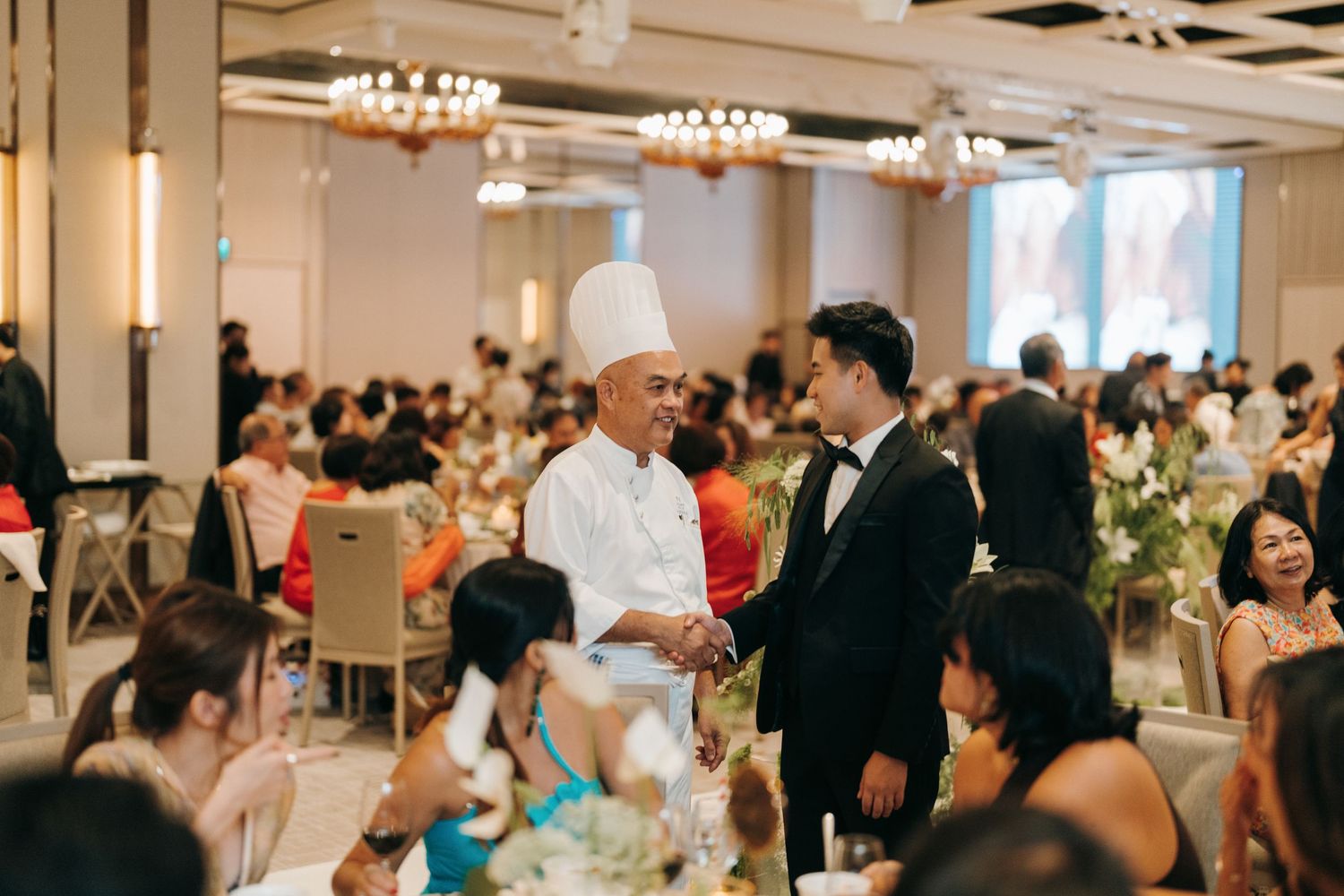 Wedding reception venue with elegant table settings and mingling guests in a bright indoor space.